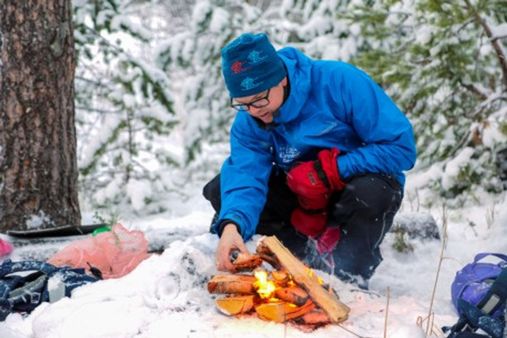 En barnehage ansatt legger mer ved på et bål i en snølagt skog.